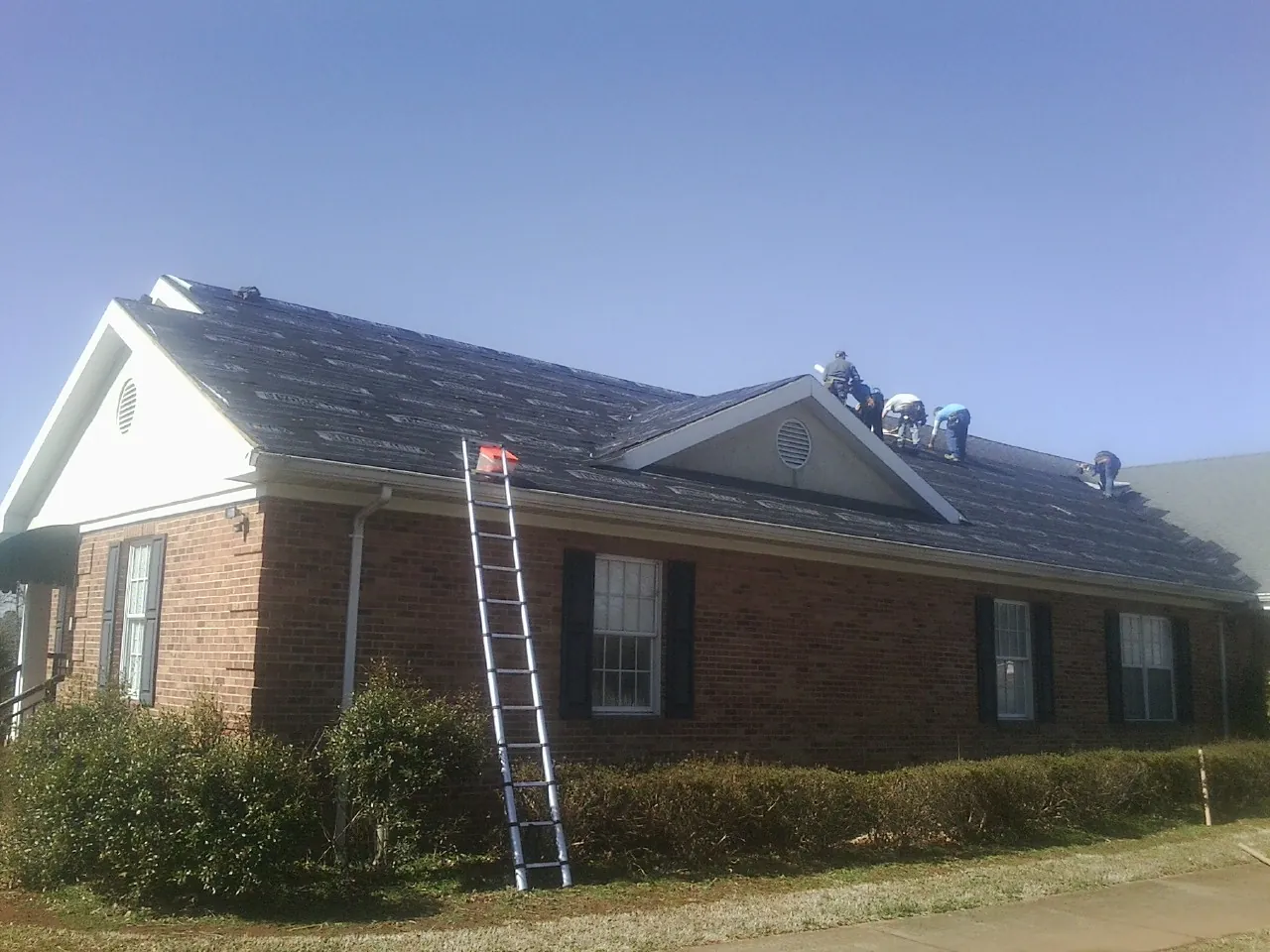 Crew tearing shingles off a brick ranch roof with a ladder set — Metal Roof Repair work by our crew in Claremont