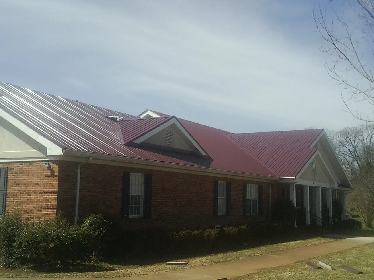 Red metal roof with gabled entries on a long brick building, from a Hail Damage Roof Repair job in Claremont