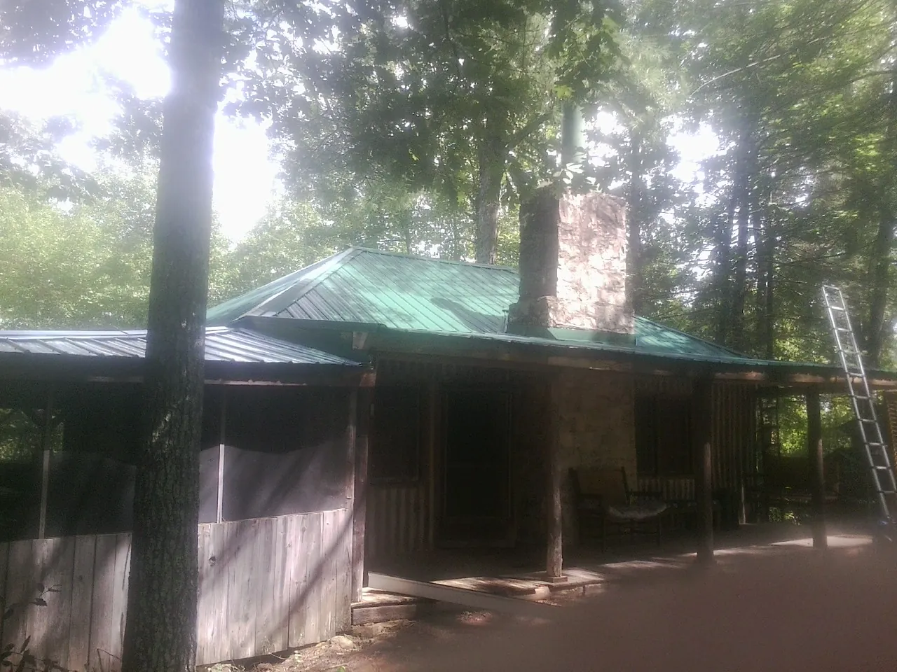 Green metal roof and stone chimney above a log cabin porch in Claremont