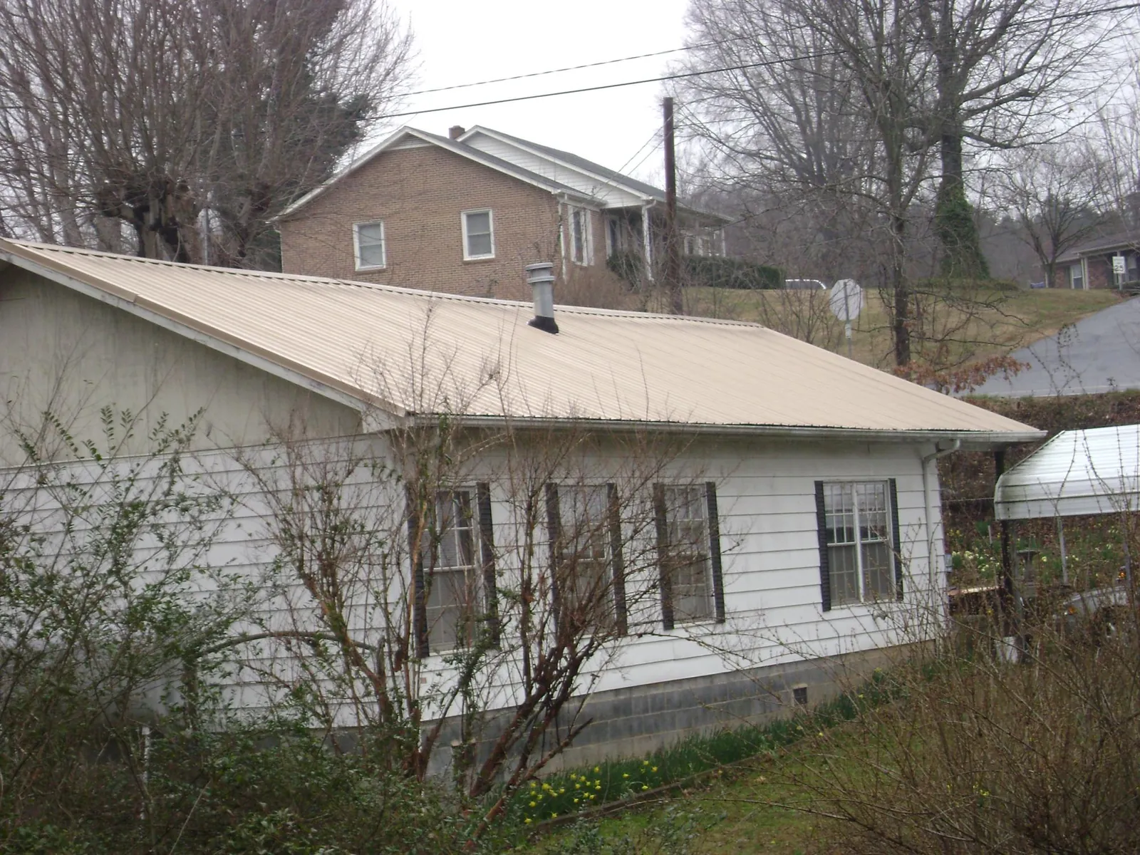Tan metal roof on a white sided house set into a hillside — Commercial Roofing by Roofing Brothers in Claremont